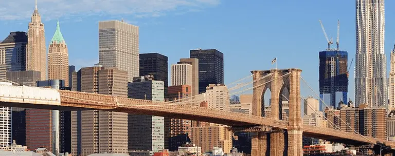 Panoramic view of Brooklyn Bridge with Manhattan skyscrapers under clear blue sky.