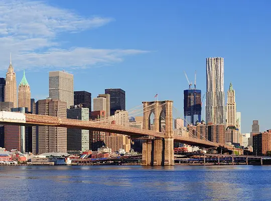 Panoramic view of Brooklyn Bridge with Manhattan skyline under clear blue sky.