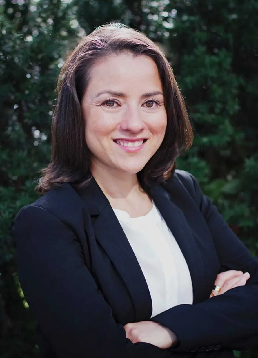 Professional woman with brown hair, wearing a black blazer and white blouse, smiling outdoors.