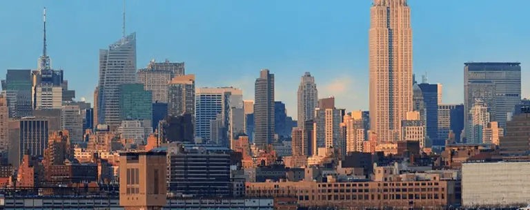 Panoramic view of New York City skyline at sunset with prominent skyscrapers and clear blue sky.