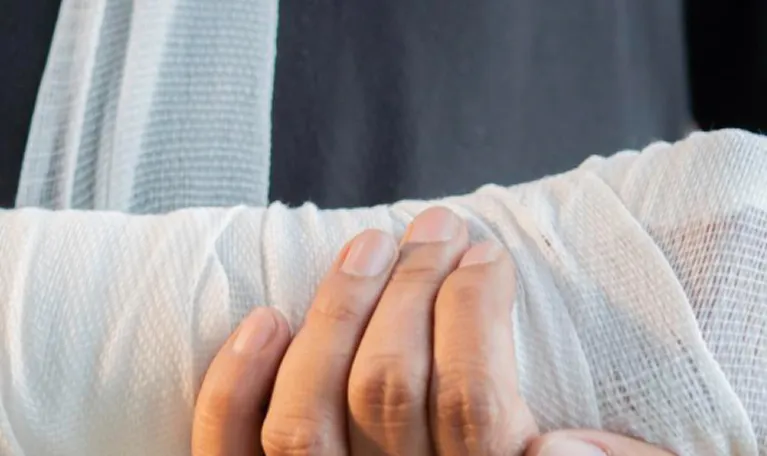 Close-up of a hand gently holding a white bandaged arm against a dark background.
