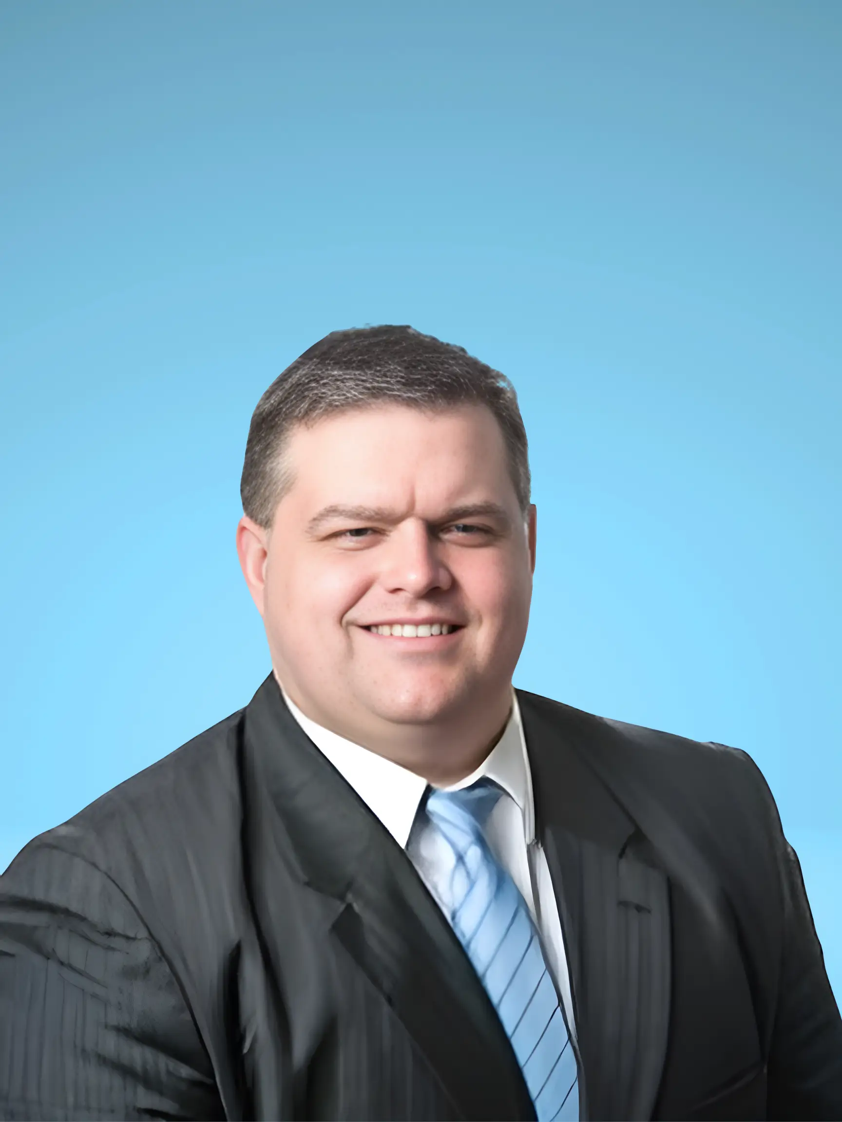 Portrait of a smiling man in a black suit and light blue tie against a blue background.