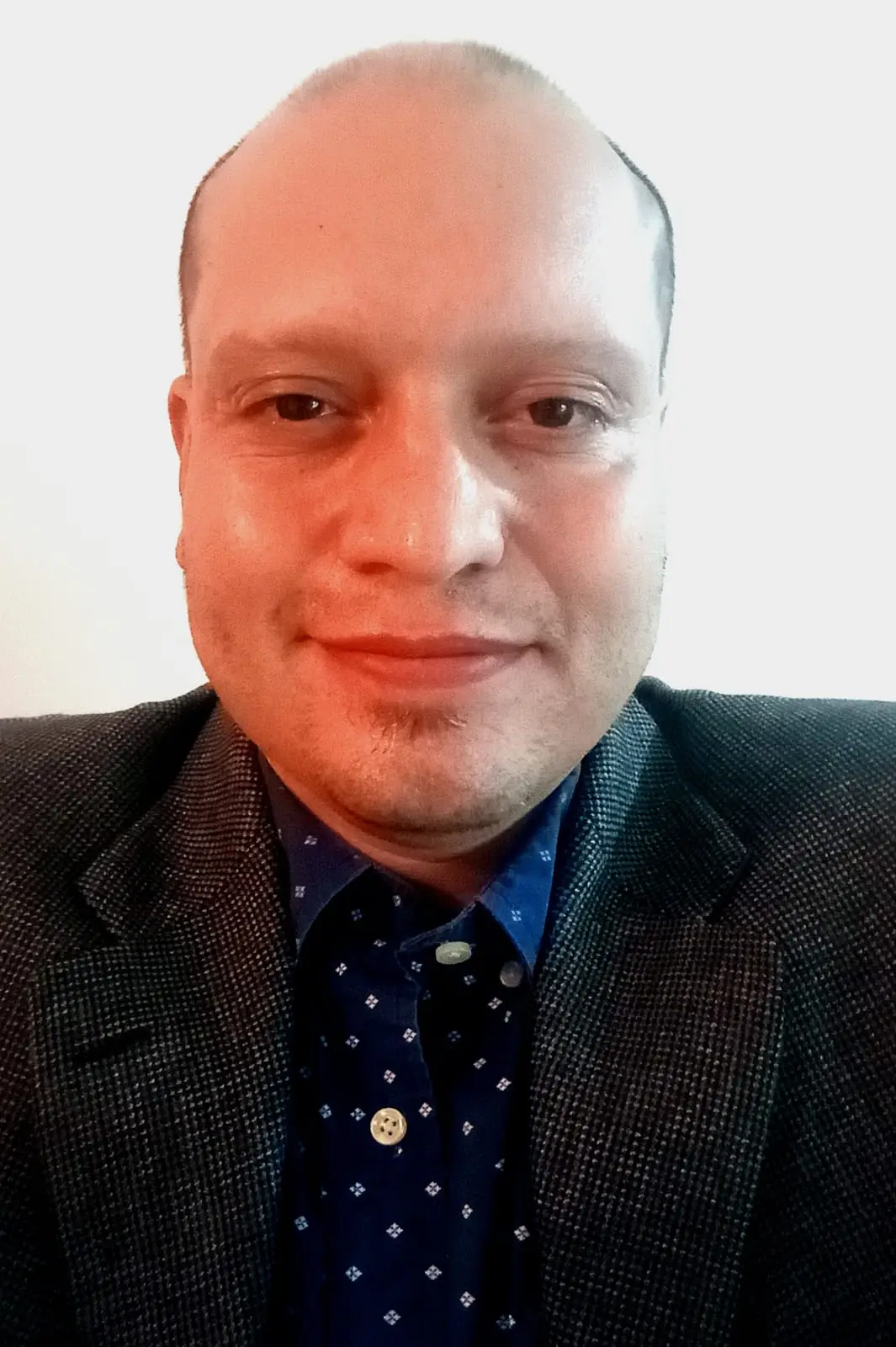 Portrait of a man wearing a dark blazer and patterned blue shirt against a plain white background.