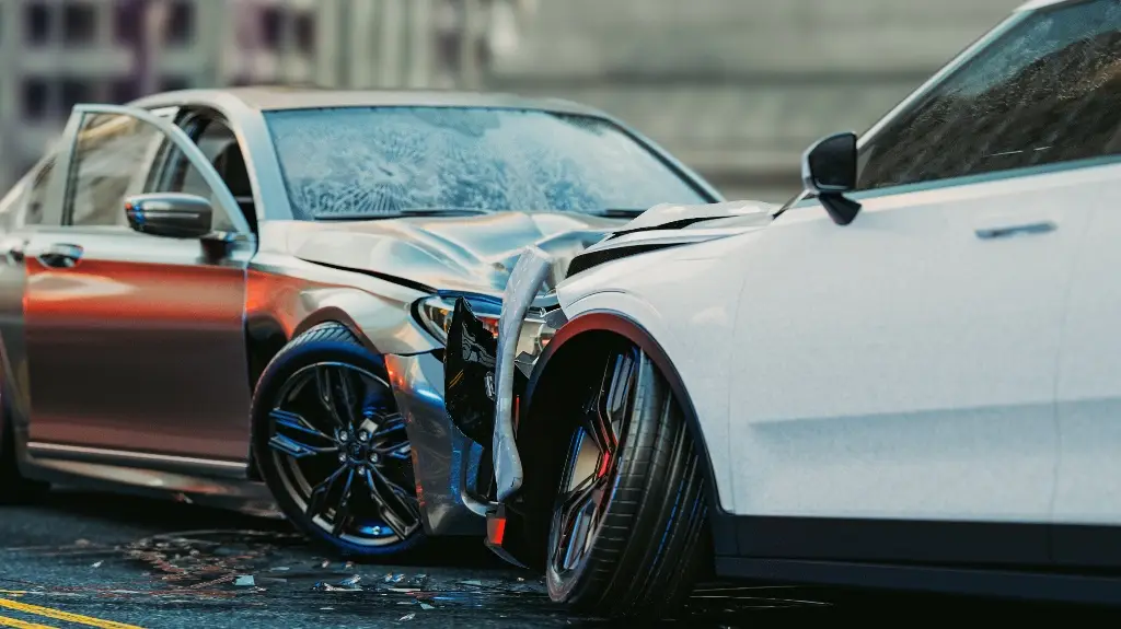 Two damaged cars, one silver and one white, involved in a front-end collision on a street.