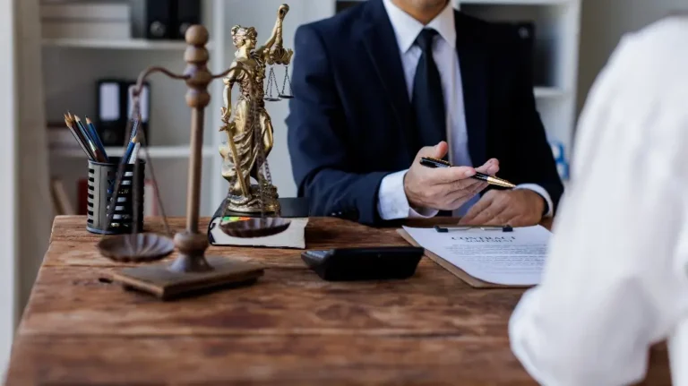 Two individuals in a legal consultation setting with a contract, scales of justice, and Lady Justice statue on a wooden desk.