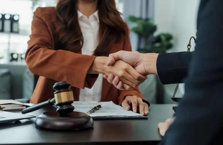 Two professionals shaking hands over a desk with legal documents and a judge's gavel.