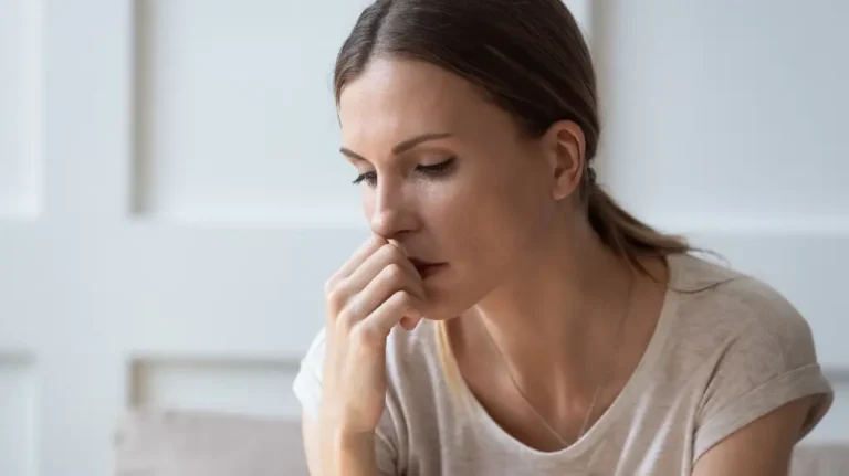 Pensive woman with brown hair in a beige shirt resting her chin on her hand.