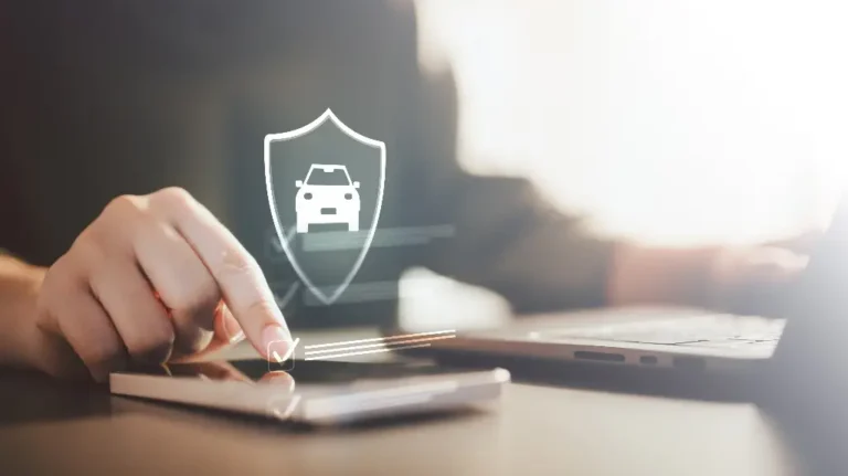 Person using smartphone with digital car insurance shield icon and checkmark, laptop nearby.
