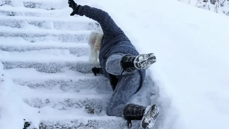 Person wearing dark winter clothing slipping and falling on snow-covered outdoor stairs.