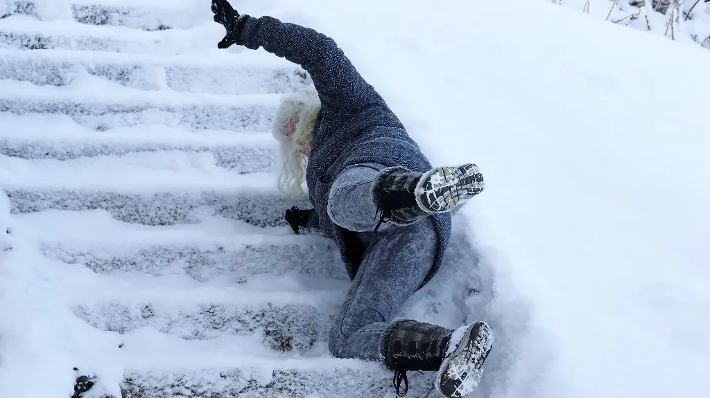 Person wearing dark winter clothing slipping and falling on snow-covered outdoor stairs.