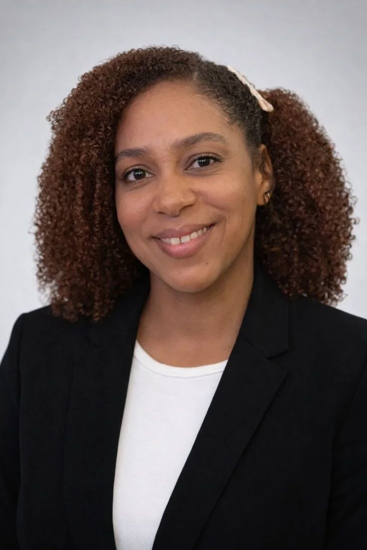 Professional portrait of a smiling woman with curly hair, wearing a black blazer and white top.